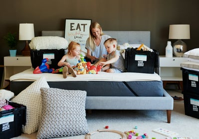 Family moving into a new home, mom sitting on a bed with kids playing with toys